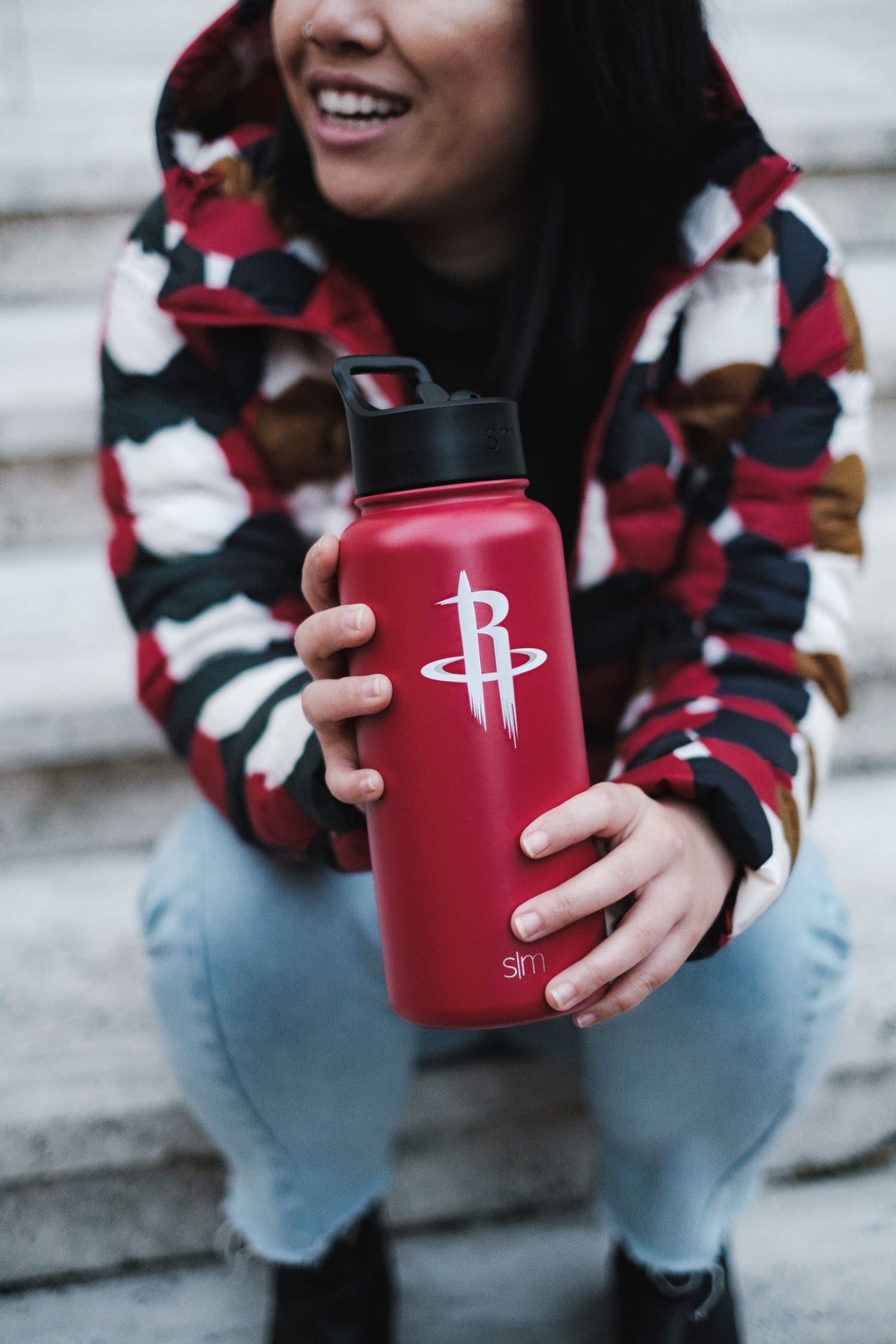 Red water bottle in foreground with person wearing navy blue and cream jacket in background against matching color palette.