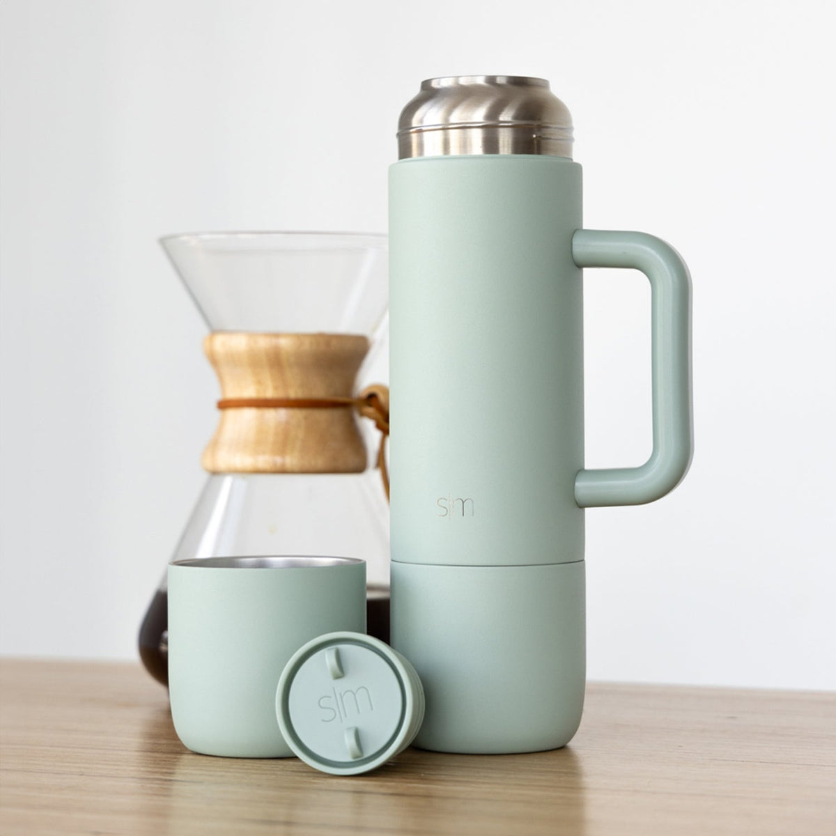 Sage green insulated tumbler with handle, matching cup, and circular lid on a neutral background