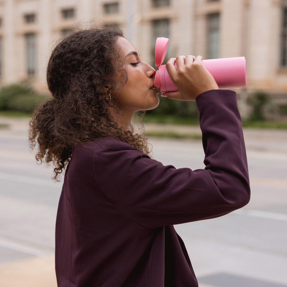 Vibrant pink tumbler held by person wearing deep plum jacket against muted background
